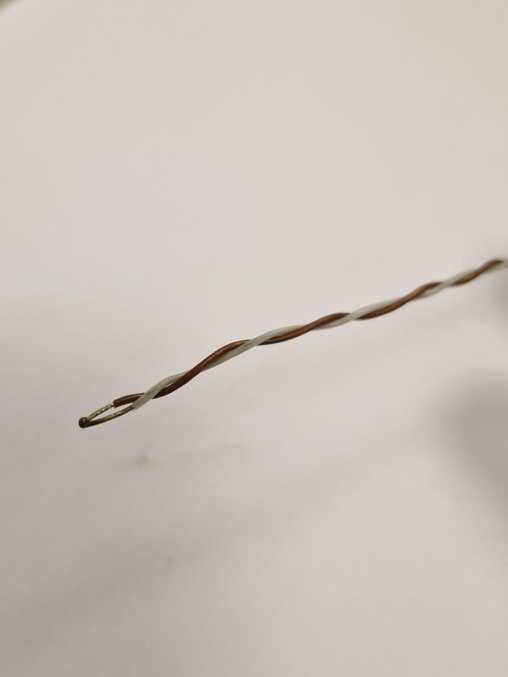 Image shows a newly welded thermocouple which consists of two wires adjoined by a weld at the tip.